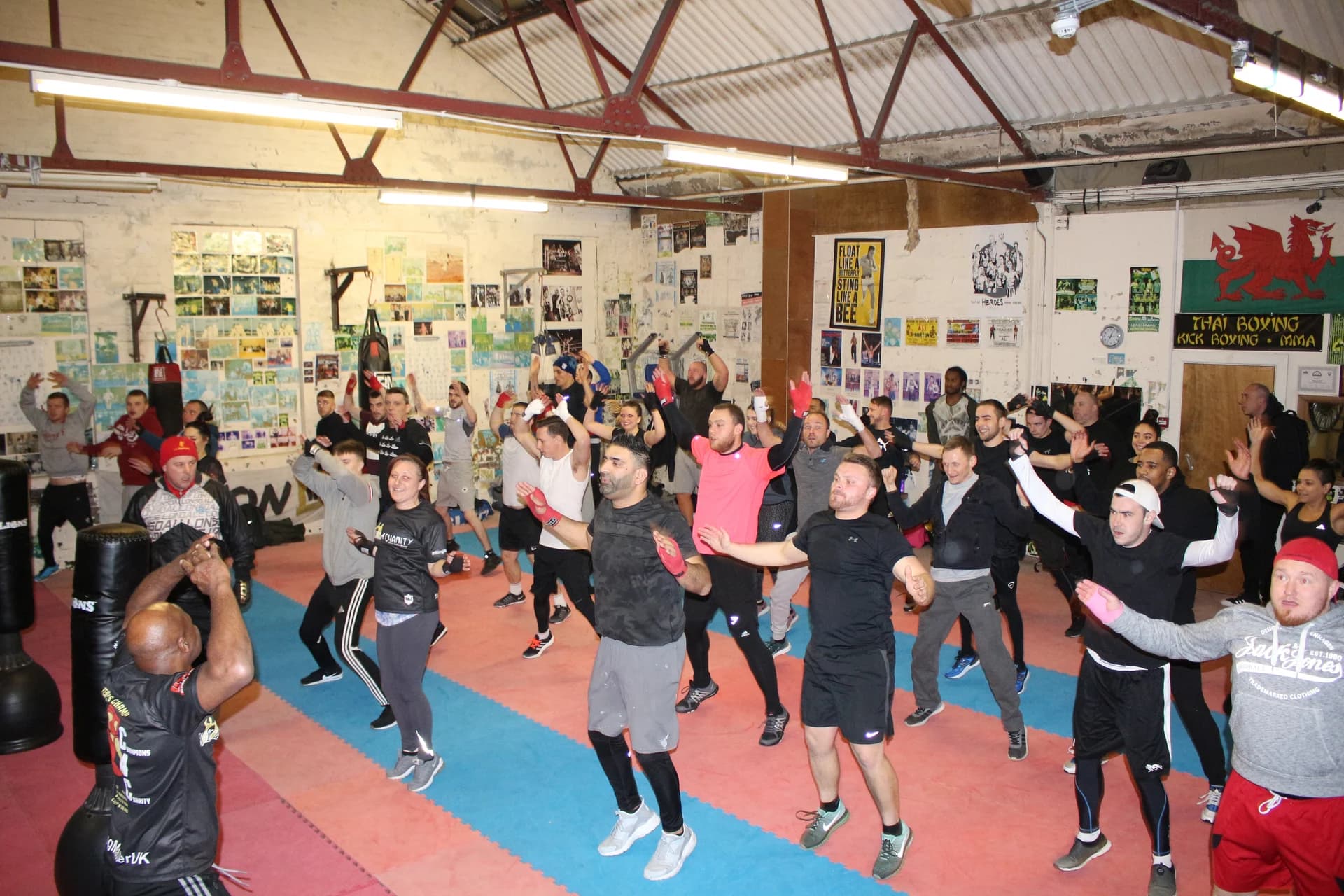 A coach leading a group warm-up with raised arms on the mats at UFCC