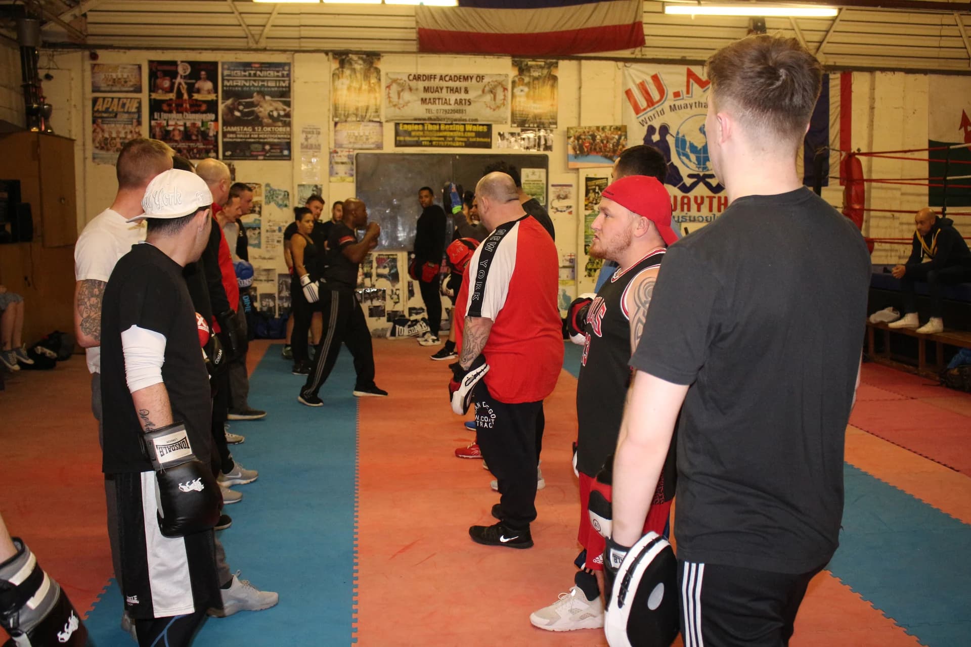 Boxing participants lined up with gloves and pads listening to a coach at UFCC