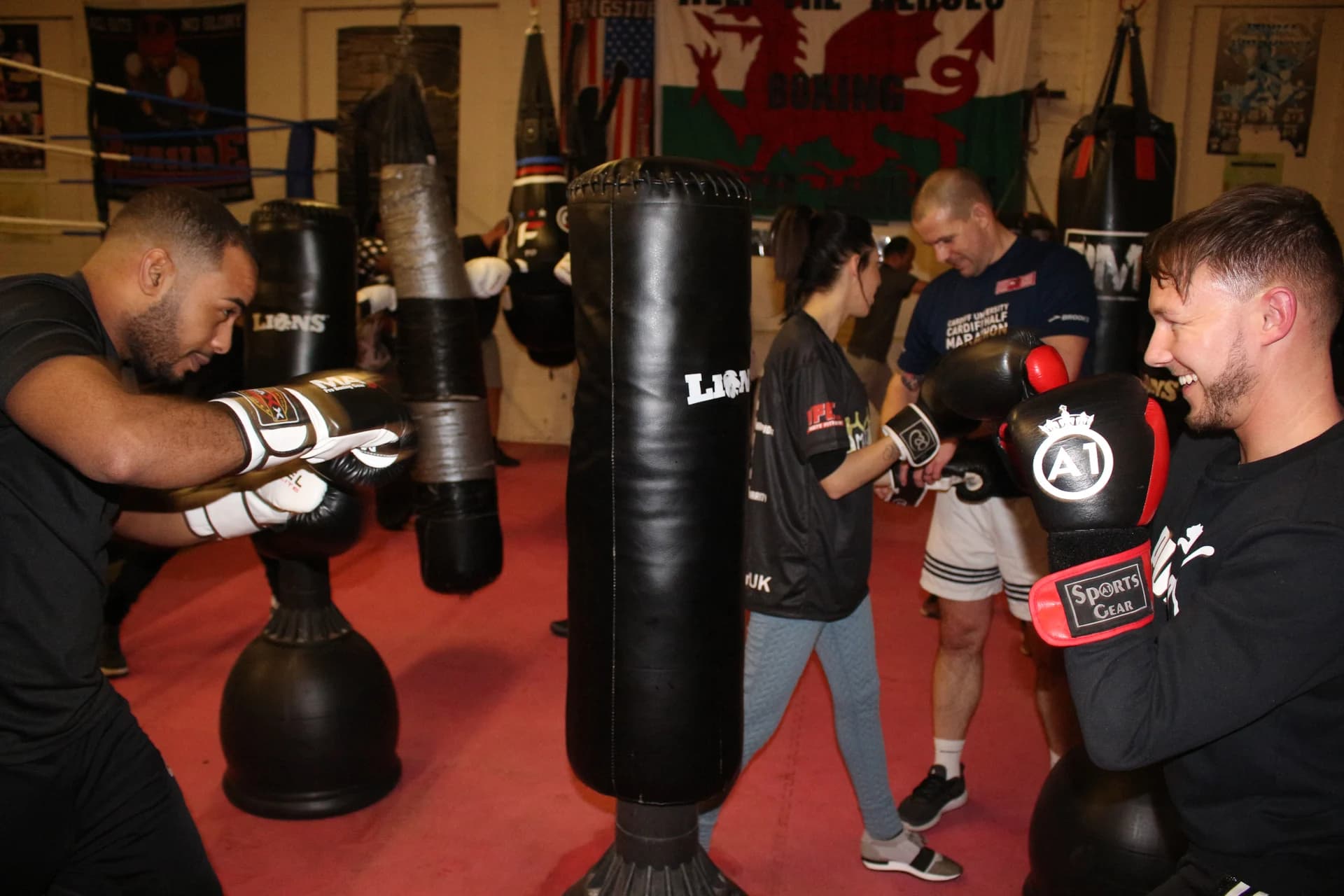Pairs practising boxing punches with focus pads beside the bags at UFCC